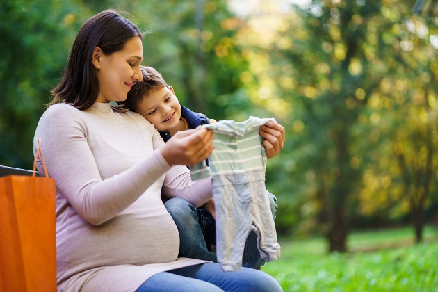 mama-insarcinata-care-se-uita-fericita-la-un-costumas-de-bebelus-si-sta-alaturi-de-baietelul-ei