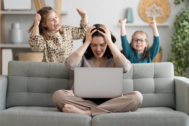 mama-stand-pe-canapea-cu-laptopul-in-timp-ce-copiii-ei-nu-o-lasa-in-pace