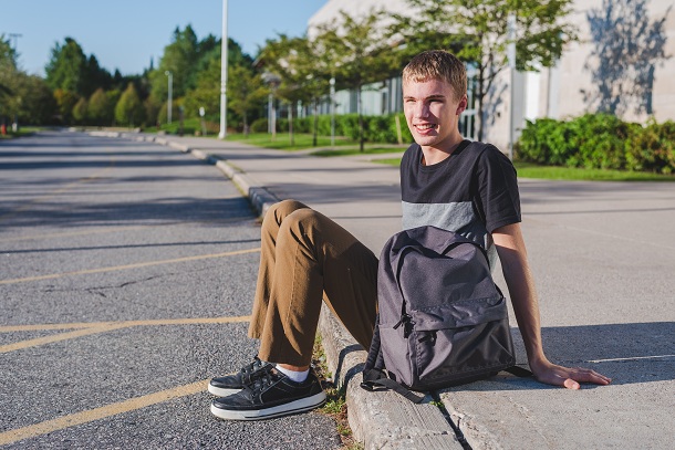 adolescent-care-sta-pe-asfalt-si-care-este-imbacat-cu-un-tricou-gri-cu-negu-si-pantaloni-maro