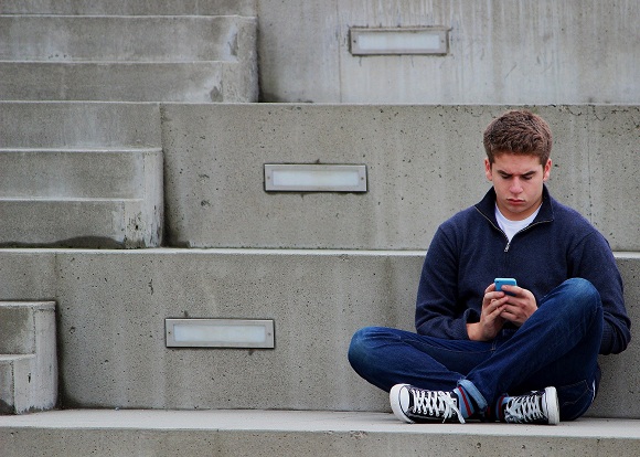 adolescent-in-blugi-care-sta-pe-asfalt-si-se-uita-pe-telefon