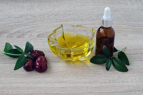 fruct-de-jojoba-ulei-de-jojoba-intr-un-castronel-transparent-si-un-recipient-langa-care-se-afla-frunze-de-jojoba