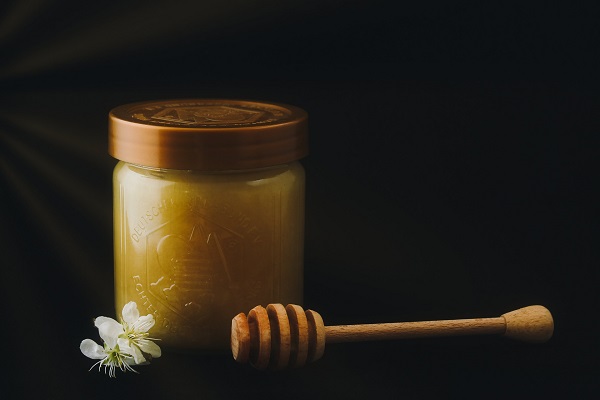 borcan-de-miere-alaturi-de-un-dispozitiv-de-lemn-pentru-servirea-mierii-si-de-o-floricica-alba
