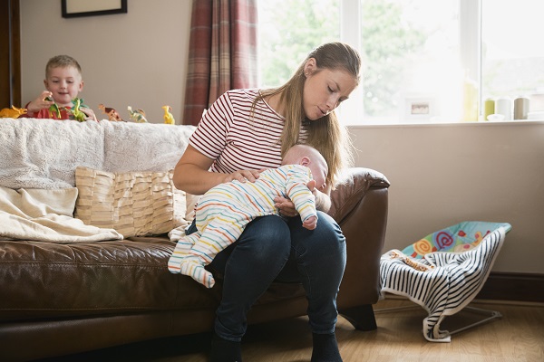 mama care sta pe marginea canapelei si il ajuta pe bebe sa ragaie