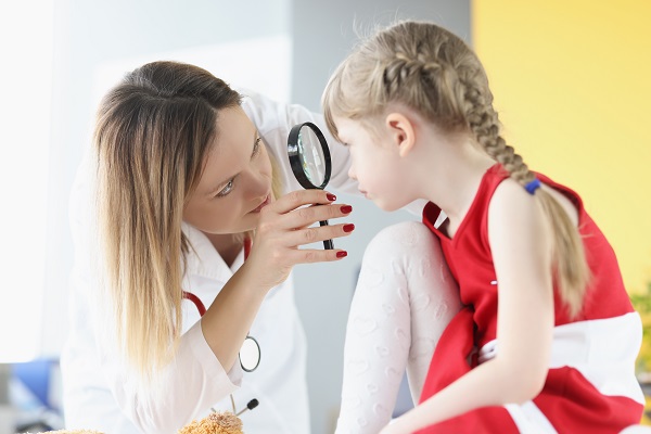 medic oftalmolog ce examineaza ochii unei fetite cu ajutorul unei lupe
