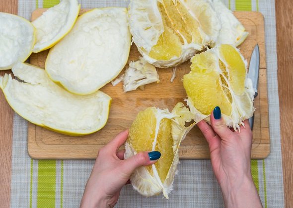 maini de femeie care curata un pomelo