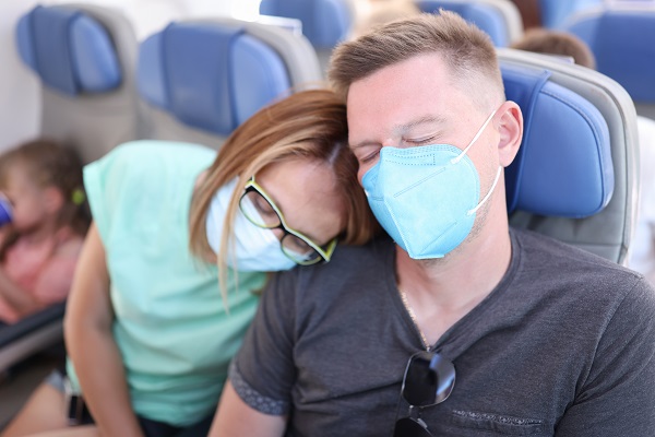 cuplu cu masti de protectie dormind in avion