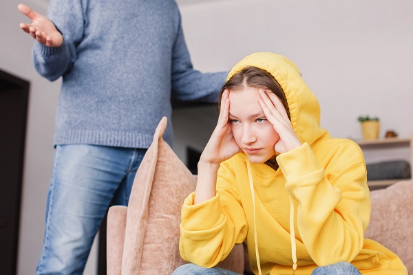 adolescenta purtand pe cap gluga unui hanorac galben in timp ce tatal ei încearca sa discute cu ea