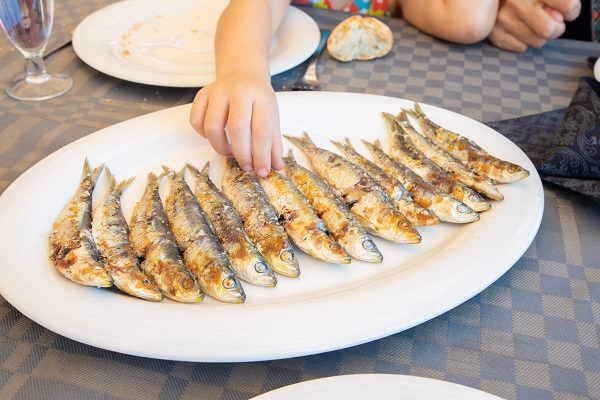 copil care se serveste cu sardine prajite de pe un platou mare alb