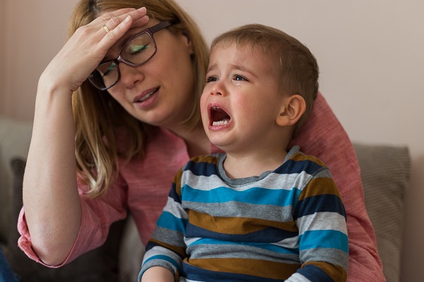 mama deprimata si ingrijorata in timp ce isi tine in brate baietelul care plange