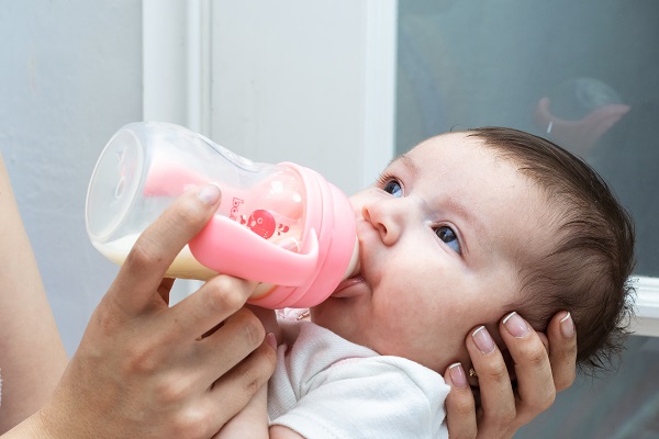 mama care isi hraneste bebelusul folosind un biberon roz