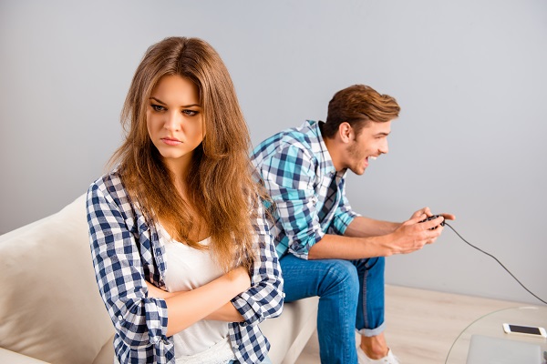 femeie tanara trista in timp ce partenerul ei sta si se distreaza pe canapea jucandu-se jocuri video