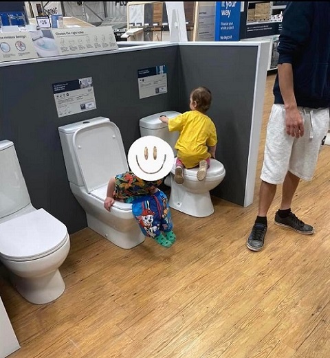 baietel stand pe un vas de toaleta dintr-un showroom si langa el stand un alt copil pe alt vas de toaleta