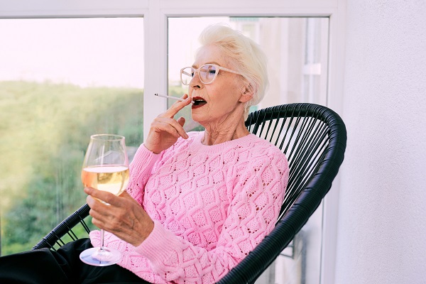 femeie in varsta eleganta cu pulover roz fumand si tinand in mana un pahar de vin