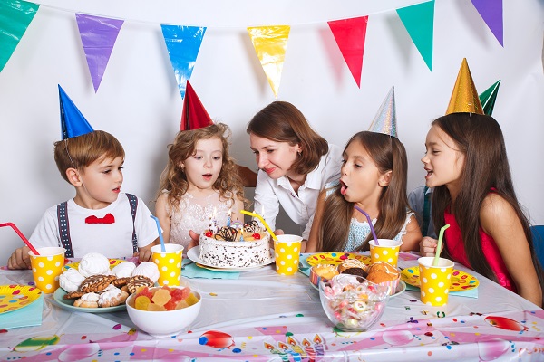 mama care aduce tortul fiicei sale la petrecerea aniversara, sarbatorita incearca sa sufle in tort, la fel si una dintre invitate