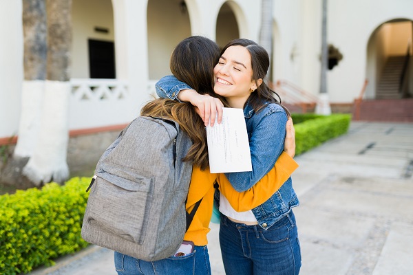 doua adolescente care se imbratiseaza dupa primirea rezultatelor de la un examen