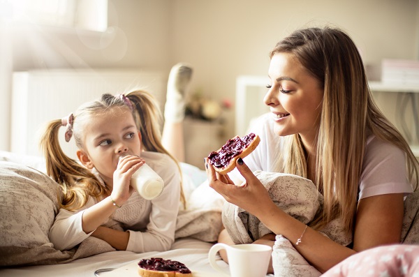 mama si fiica iau micul dejun fetita bea doar lapte, iar mama mananca paine cu gem