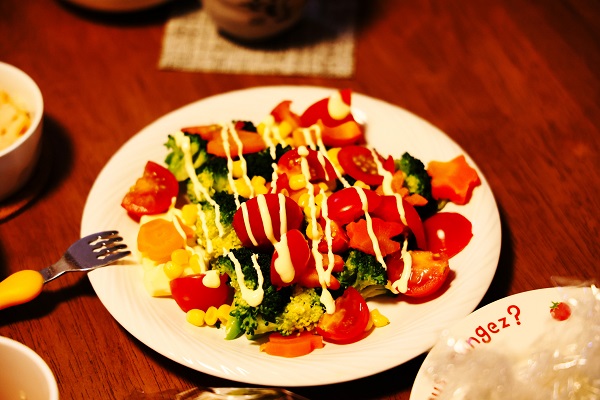 salata cu broccoli, morcovi, rosii, porumb si maioneza pe o farfurie alba