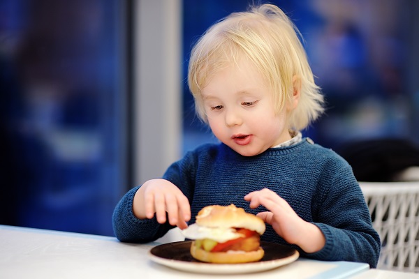 baietel blond care sta la masa si vrea sa manance un hamburger