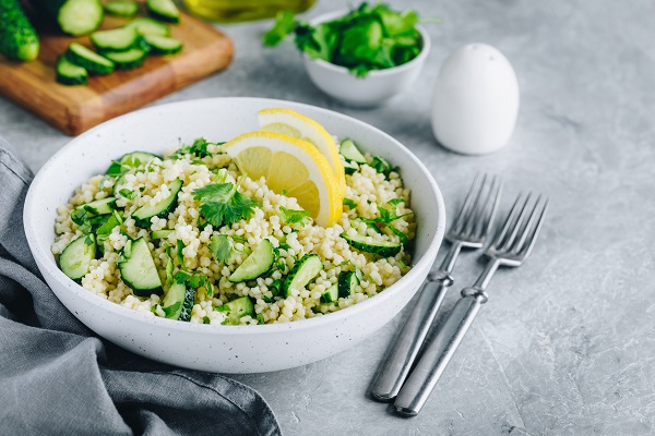 castron alb cu salata de couscous, castraveti, decorata cu o felie de lamaie si cu frunze de patrunjel