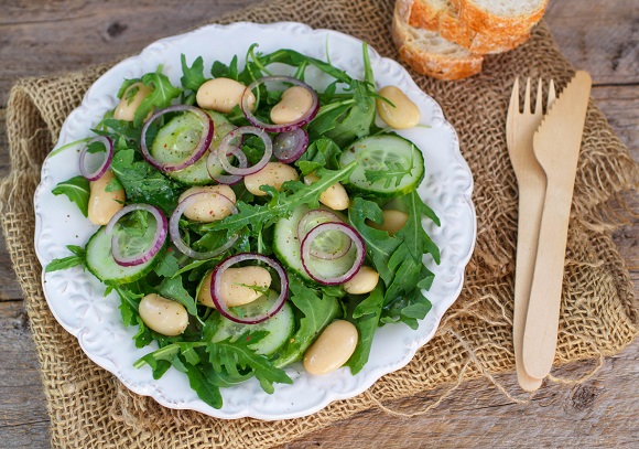 farfurie alba cu salata cu ruccola, boabe de fasole, ceapa rosie si rondele de castraveti