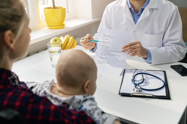 medic nutritionist care îi arata unei mame cu bebelus in brate o lista cu dieta de care sa tina cont