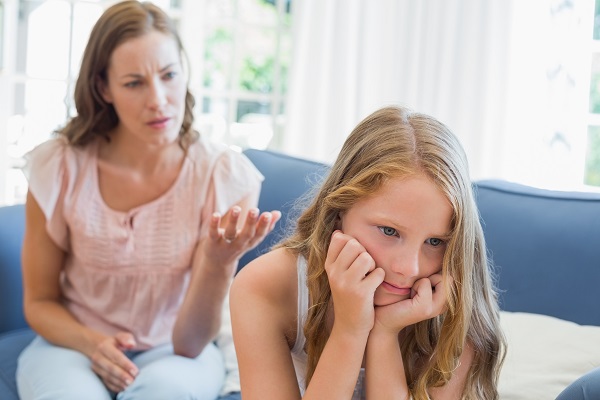 fetita suparata care sta pe canapea in timp ce mama sa e in spatele ei si îi face observatii