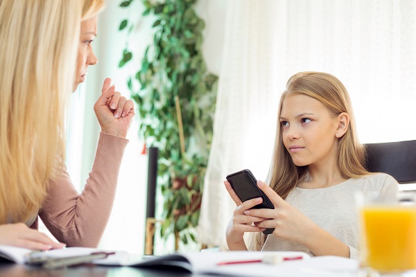 adolescenta iritata care sta pe telefon in fata mamei ei