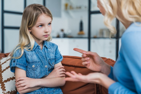 fetita in tinuta din jeans stand trista pe o canapea in timp ce o mama ei îi face observatii