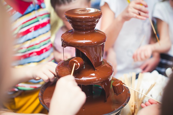 copii adunati in jurul unei fantani de ciocolata, incercand sa introduca in ciocolata bezele