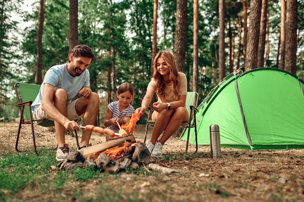 mama, tata si fetita lor pregatind ceva de mancare la foc la o iesire cu cortul in padure
