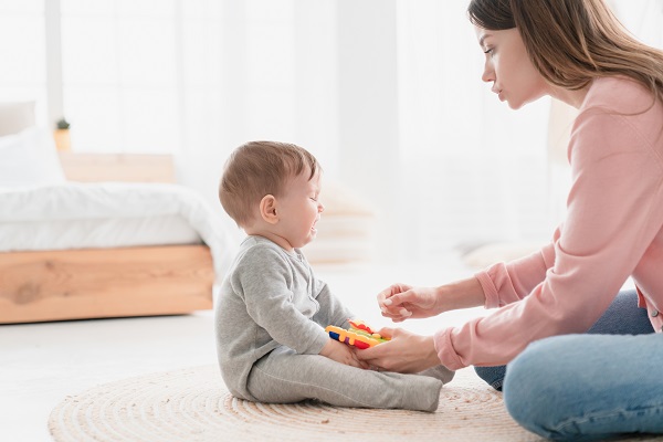 bebelus care se joaca pe podea si plange, iar mama lui incearca sa-l calmeze