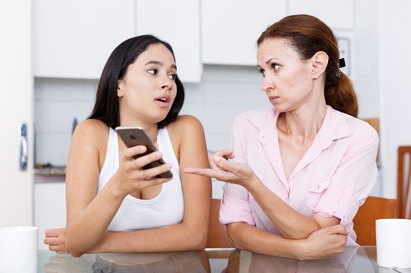 mama care incearca sa discute cu fiica ei adolescenta, care isi tine telefonul in mana