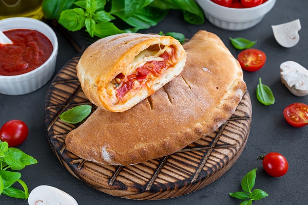 calzone rumenit si o bucata din el pe un platou de lemn