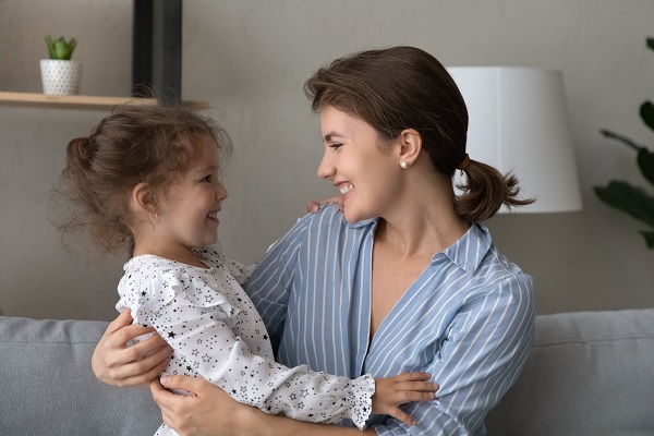 mama fericita in camasa bleu cu dungi albe uitandu-se cu dragoste si bucurie la fetita ei zambitoare