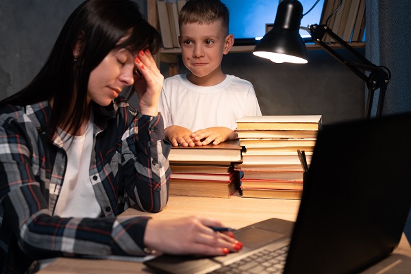 mama extenuata care lucreaza noaptea la computer in timp ce baietelul ei se uita la ea