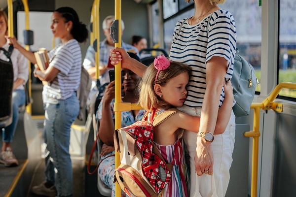 fetita cu ghiozdan in spate trista strangandu-si mama in brate in autobuz