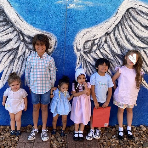 sase copii de varste diferite, in spatele lor aflandu-se un zid pictat in albastru si alb