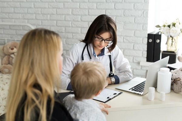 mama care isi tine baietelul in brate in cabinetul unei doctorite care scrie recomandari sau o reteta