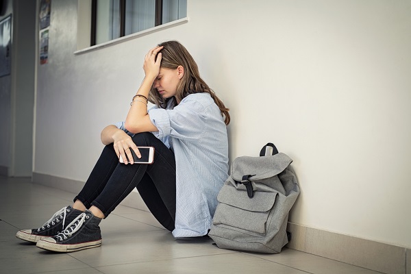 adolescenta deprimata stand pe jos si tinandu-si in mâna telefonul