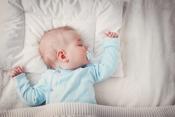 bebelus in costumas bleu care doarme linistit cu suzeta in gurita