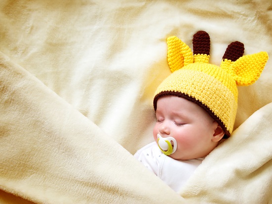 bebelus care doarme cu suzeta si o caciulita tricotata de girafa