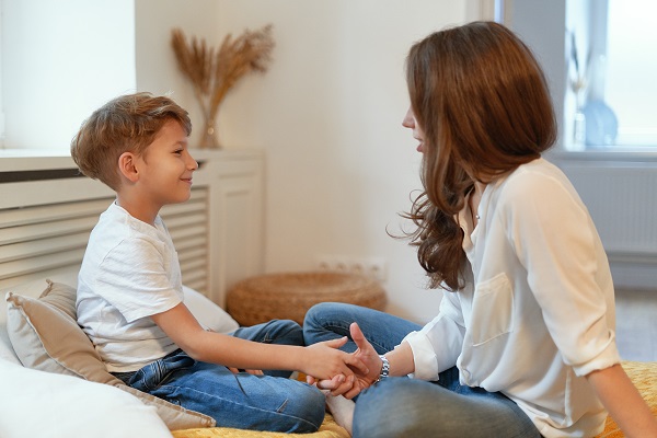 baietel care sta in pat si zambeste in timp ce mama lui îi explica ceva