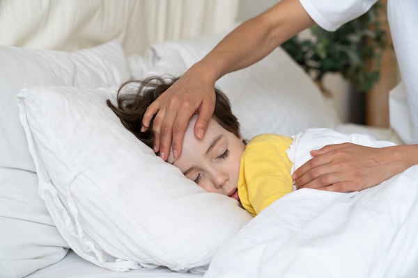 femeie care pune mâna pe fruntea unui copil care doarme pentru a verifica daca acesta are febra