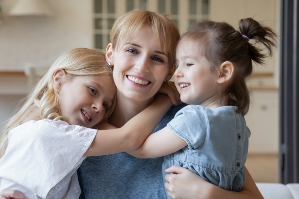 mama fericita in timp ce sta cu cele doua fetite ale sale, care o imbratiseaza