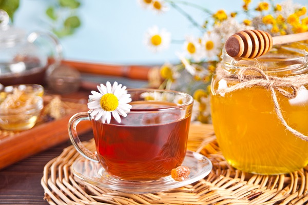 cana de ceai decorata cu o floare de musetel, langa ea aflandu-se un borcan cu miere
