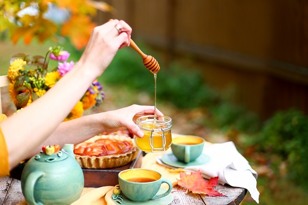 femeie ce se afla in gradina toamna, la o masa cu tarta de mere, cu cani cu ceai si care incearca sa utilizeze miere