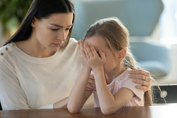 mama care incearca sa isi consoleze fetita trista ce isi acopera fata cu mainile