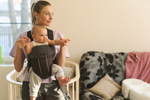 mama fericita care isi tine fetita intr-un marsupiu