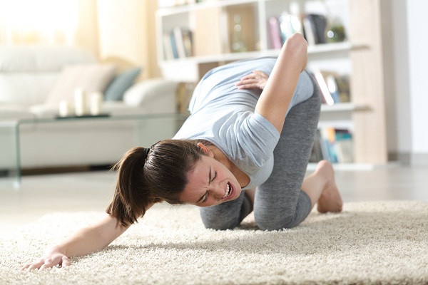 femeie tanara ce are o criza cu dureri de spate in timp ce incearca sa practice yoga acasa