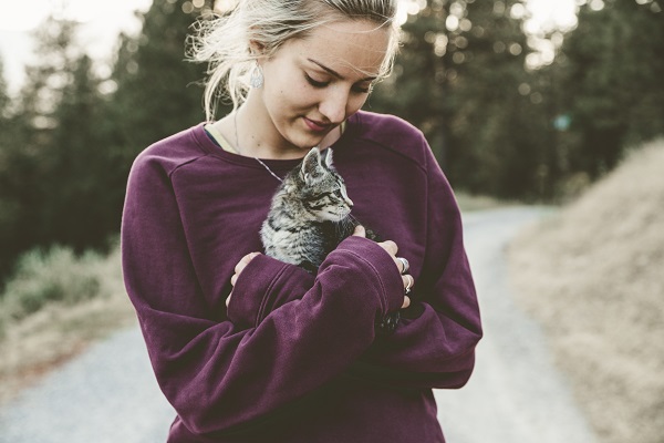 femeie tanara blonda in bluza violet tinand in brate o pisicuta 